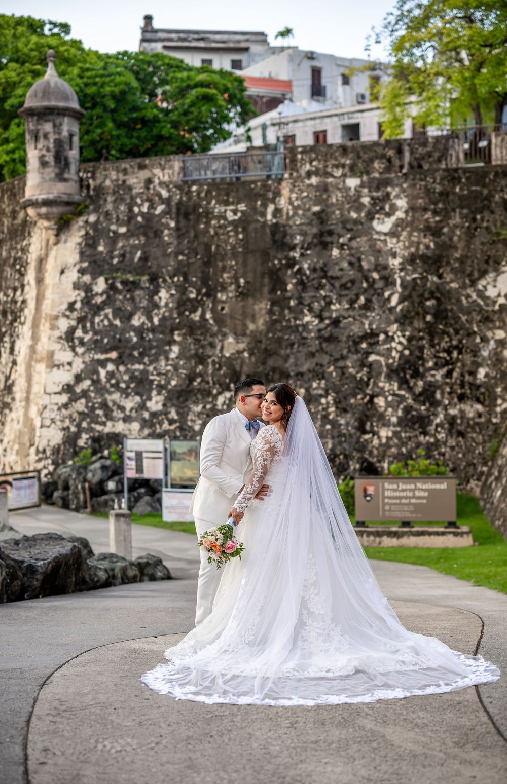 A couple poses for wedding photos in front of an old stone fortress wall at various romantic angles.
