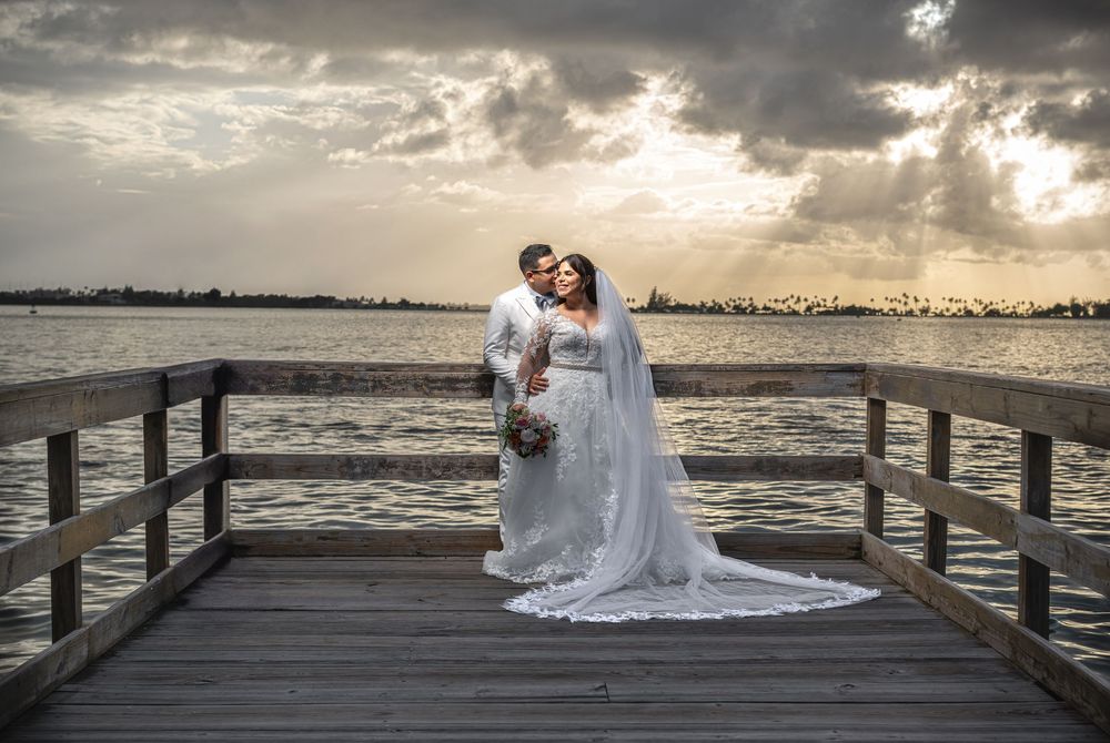 Romantic sunset silhouettes on a wooden pier overlooking the ocean with dramatic cloudy sky.