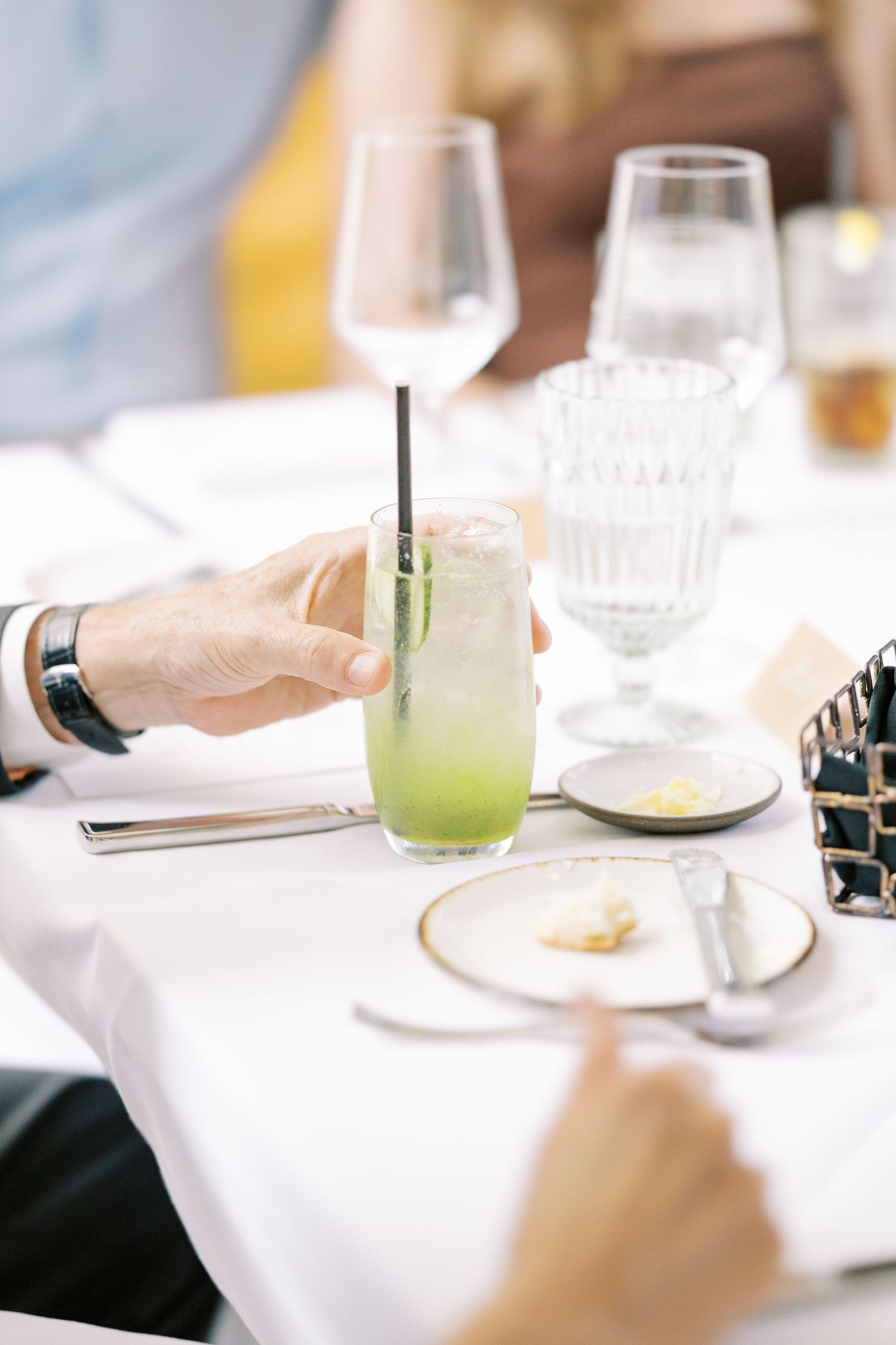 A refreshing green cocktail sits on a white tablecloth next to wine glasses and place settings at an elegant dining table at Ninety Acres.
