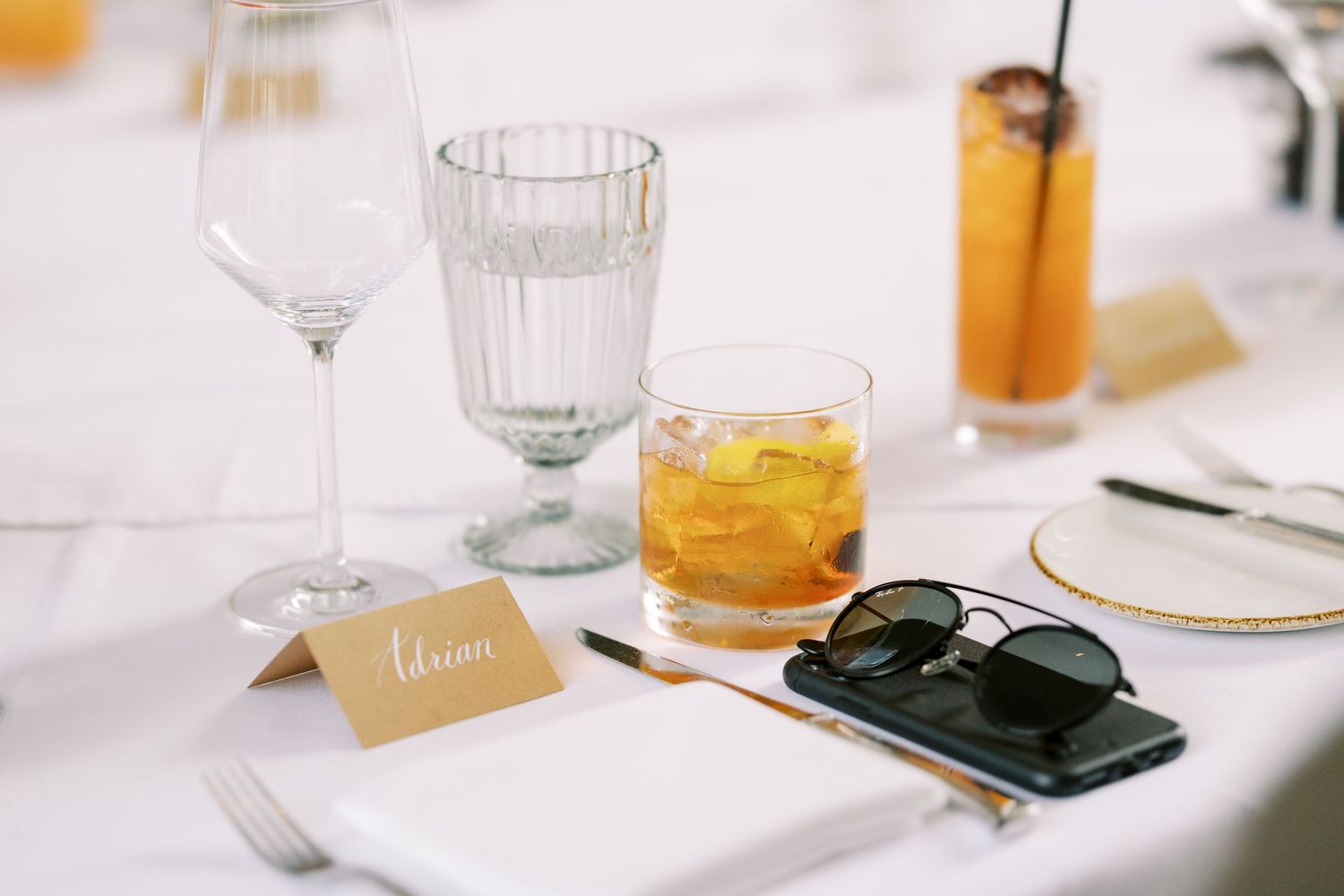 Elegant place setting at white table with cocktail, sunglasses, name card and wine glasses at Ninety Acres and Pendry Natirar.