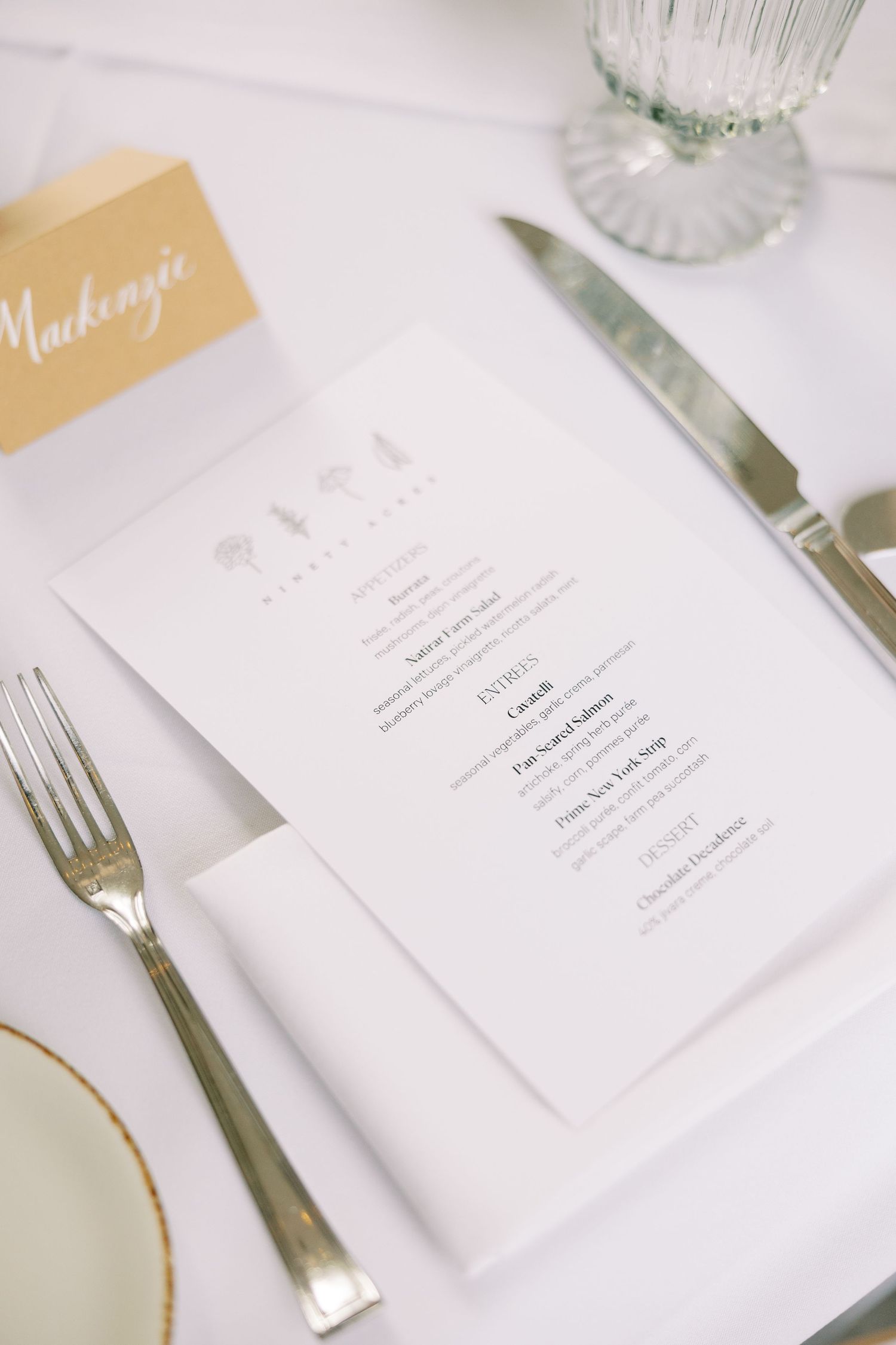 Elegant white menu cards with gold accents and silverware set against a light marble table setting at Ninety Acres and Pendry Natirar