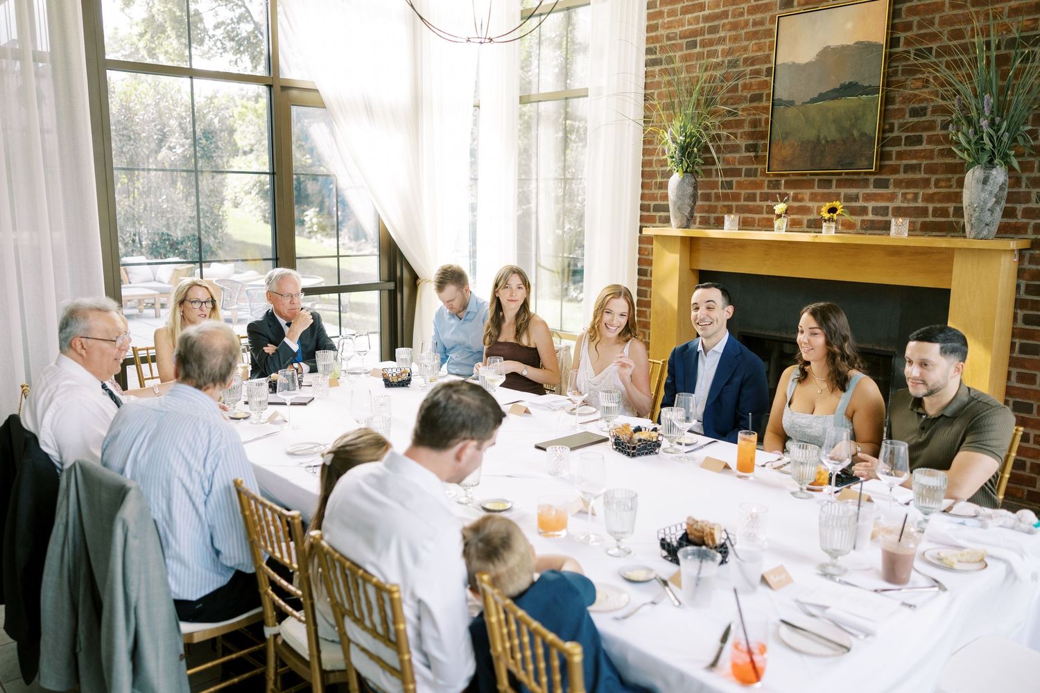 Elegant dining scene with guests gathered around a long table in a bright room with brick walls and natural light at Ninety Acres.