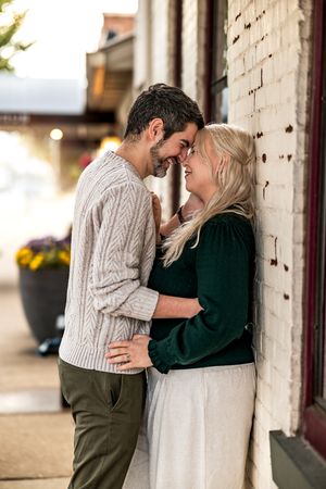 A couple shares an intimate moment leaning against a brick wall, wearing cozy sweaters on an autumn day.