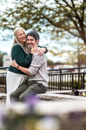 A couple shares an intimate moment while sitting outdoors, with the woman in green embracing the man in a cable knit sweater.