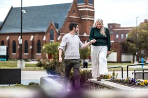 A wedding couple stands together on a cobblestone path near a stately brick church on their special day.