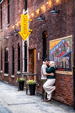 A couple admiring art displayed in a historic brick alleyway with warm lighting and vintage building details.