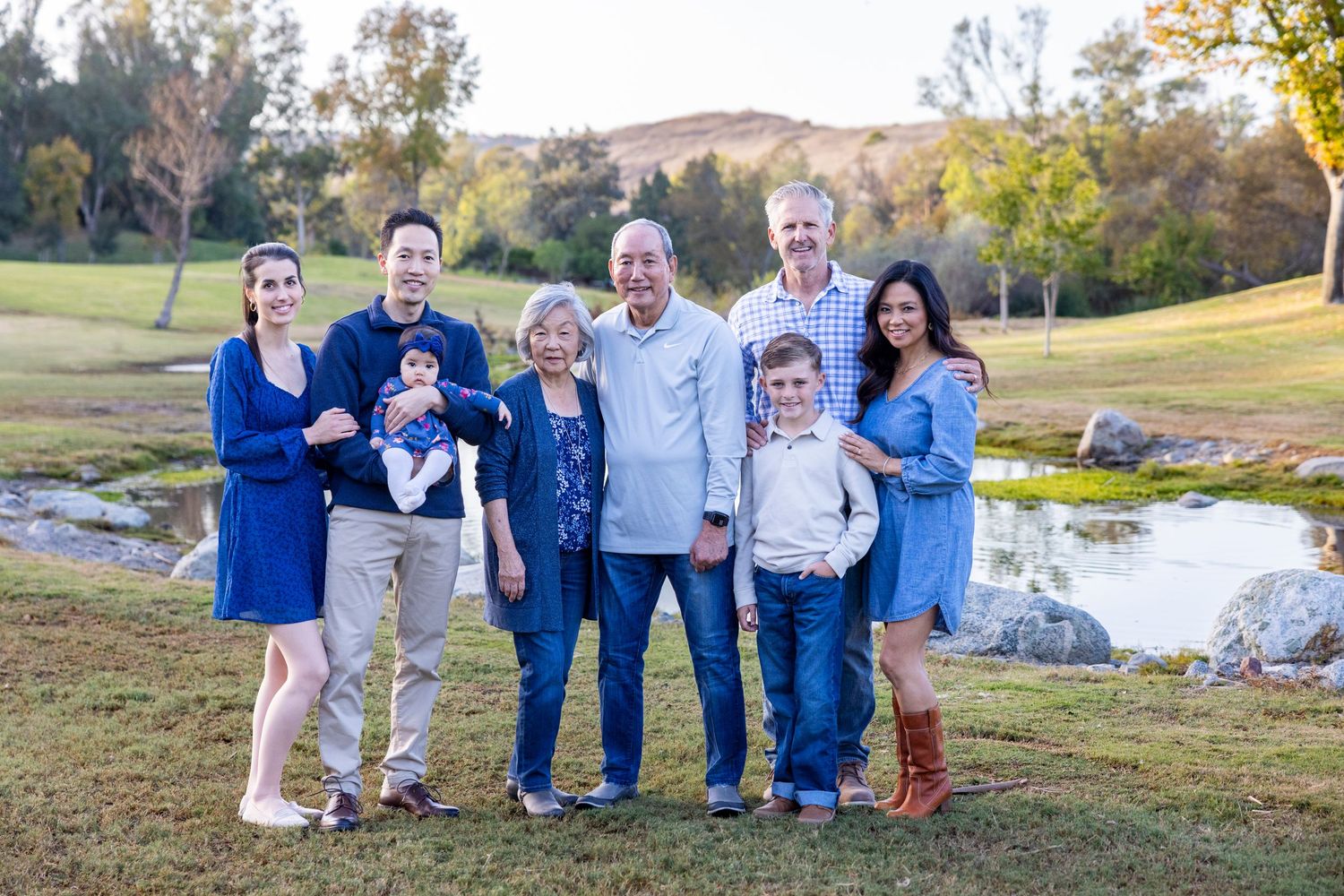 Laguna Niguel photographer captures Multigenerational family of seven smiles together on a lush golf course near a serene pond.