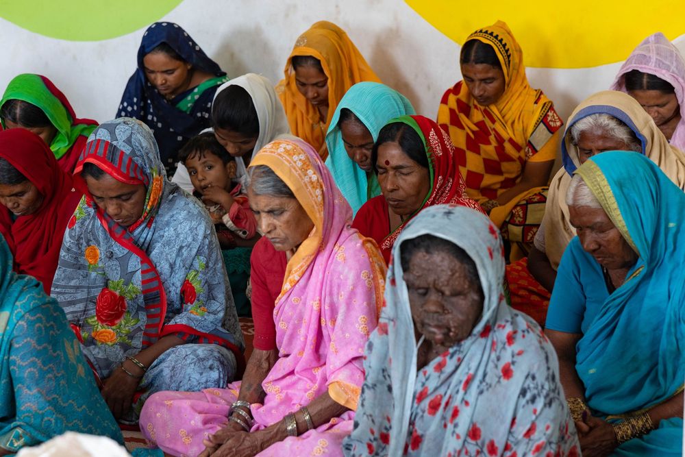 A row of women in colorful traditional saris and headscarves sit together at a community gathering.