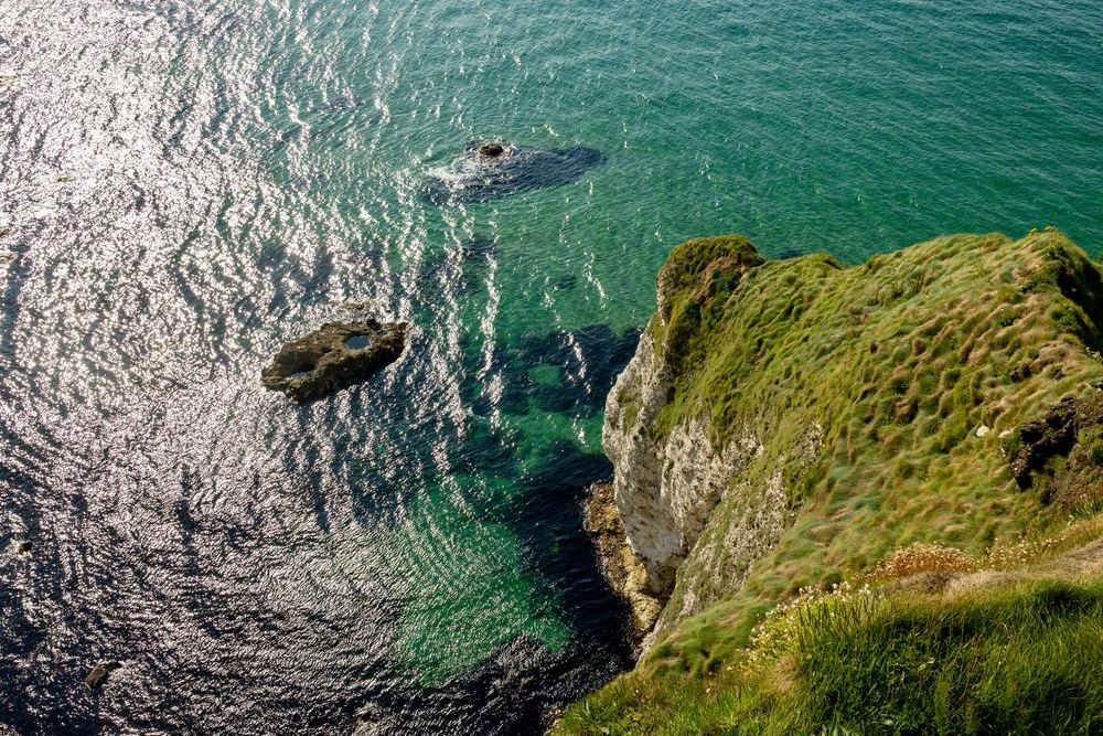 Aerial view of green coastal cliffs meeting turquoise waters with rocky outcrops in the Irish Sea.