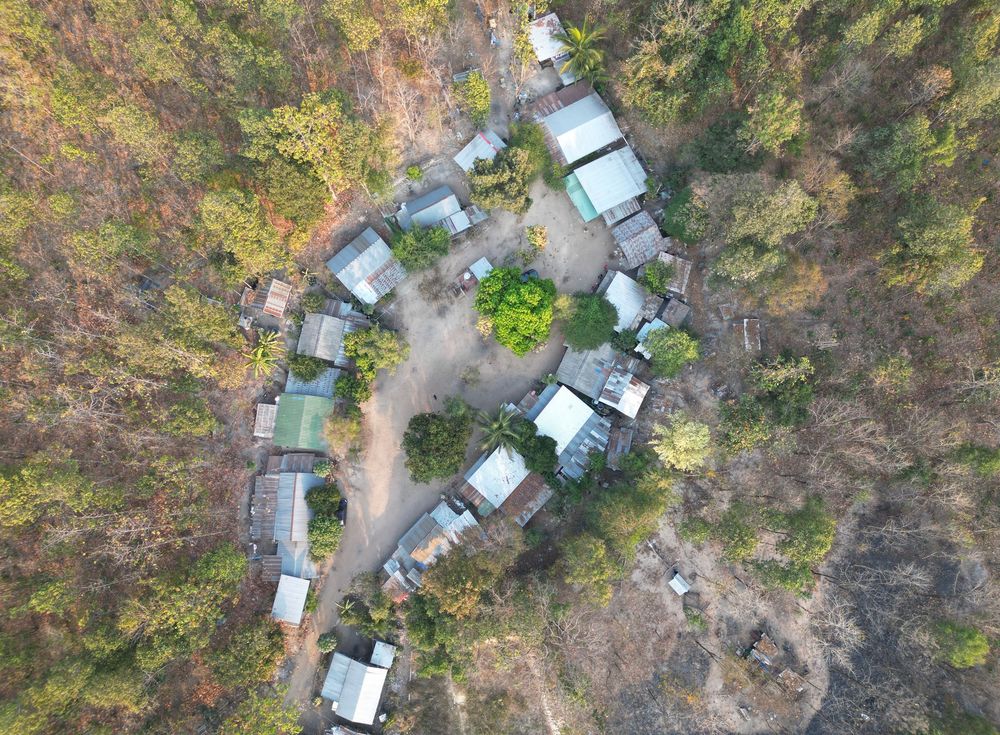 Aerial drone images reveal a small camping area with RVs and trailers nestled among autumn trees in a remote woodland setting.