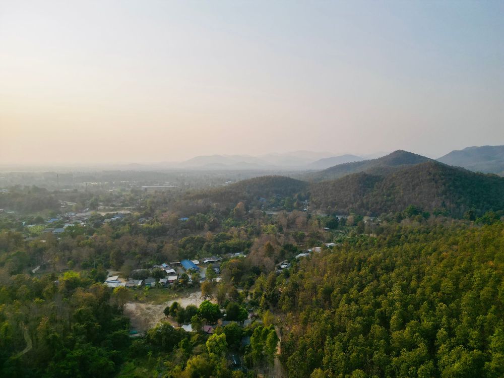 Aerial view of mountain landscape with scattered houses nestled among green forests during sunset.