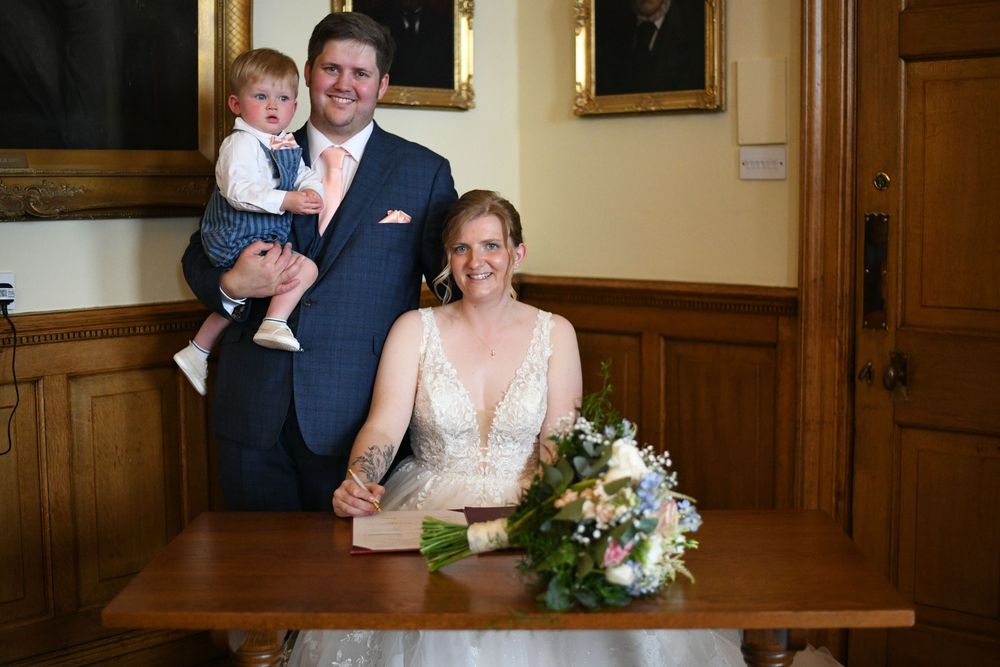 A small group gathers together at a wedding in an elegant wood-paneled room with a classic framed portrait on the wall.