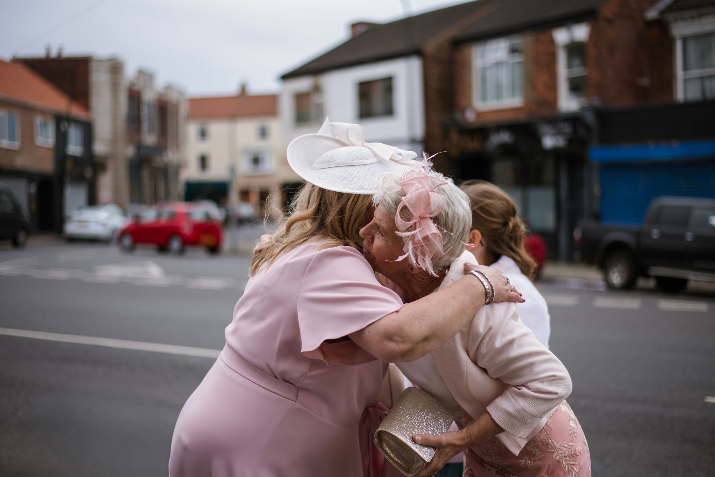 Friends embracing outdoors on a street corner in pastel pink clothing.
