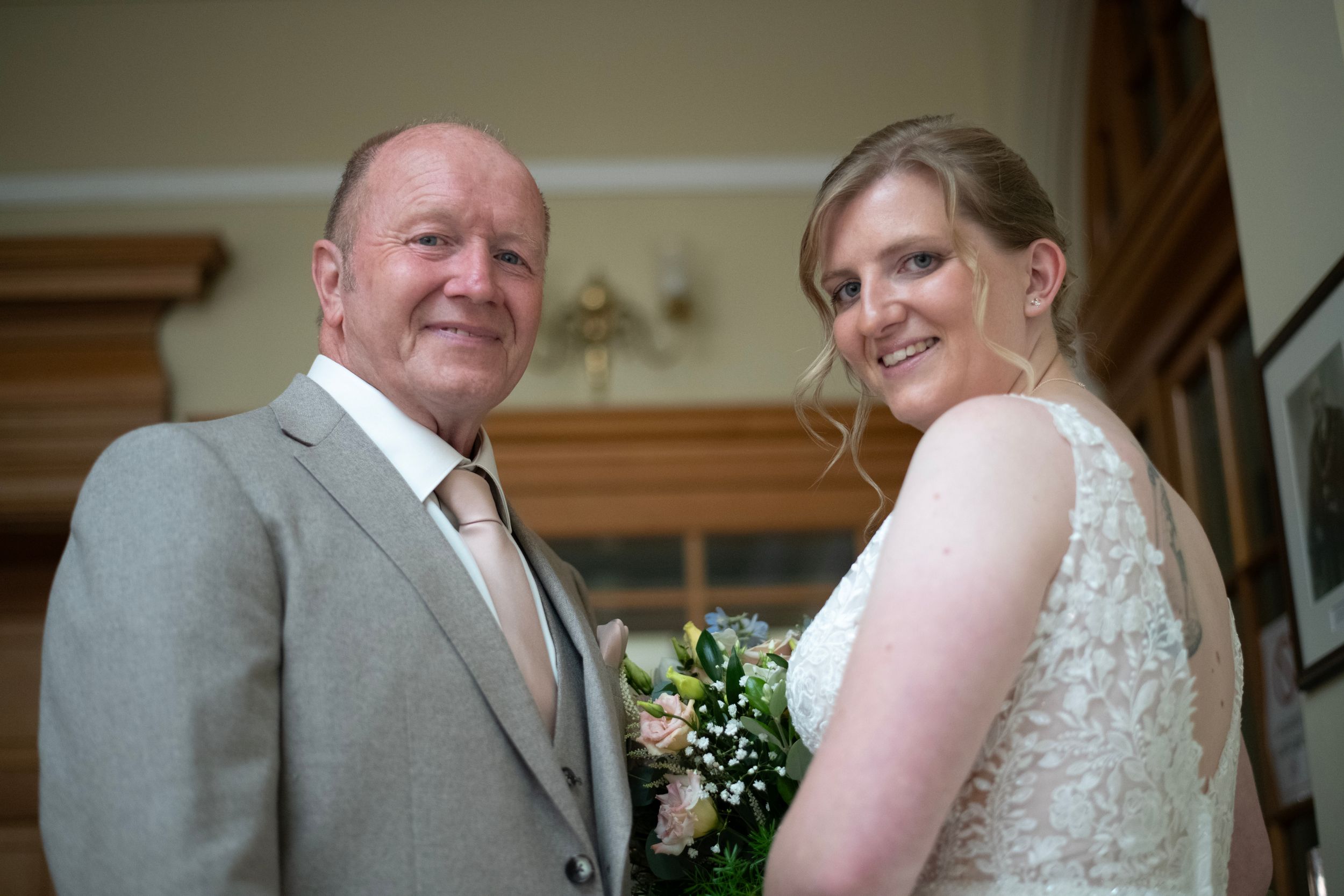 A bride and groom share a tender moment in a ceremony while wearing a gray suit and lace dress.