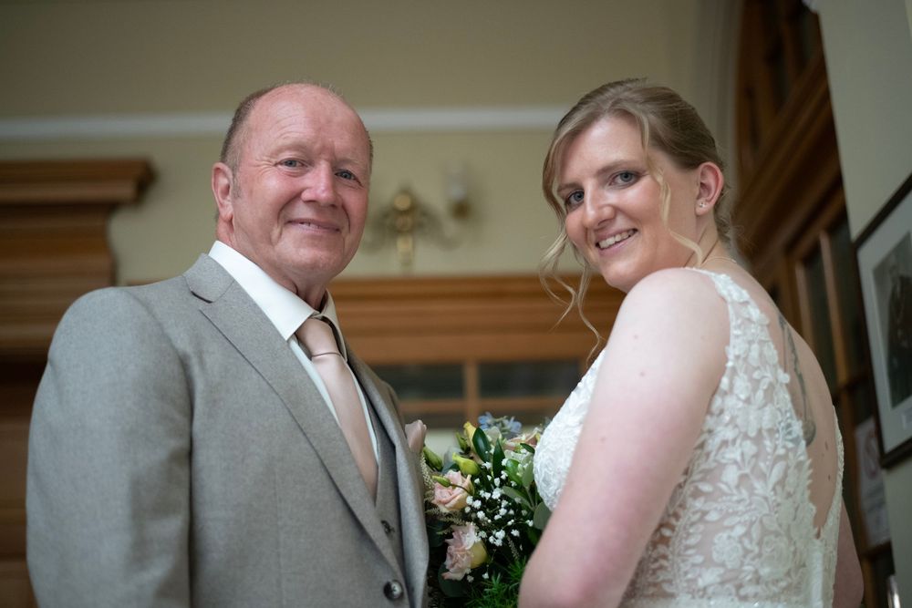 A bride and groom share a tender moment in a ceremony while wearing a gray suit and lace dress.