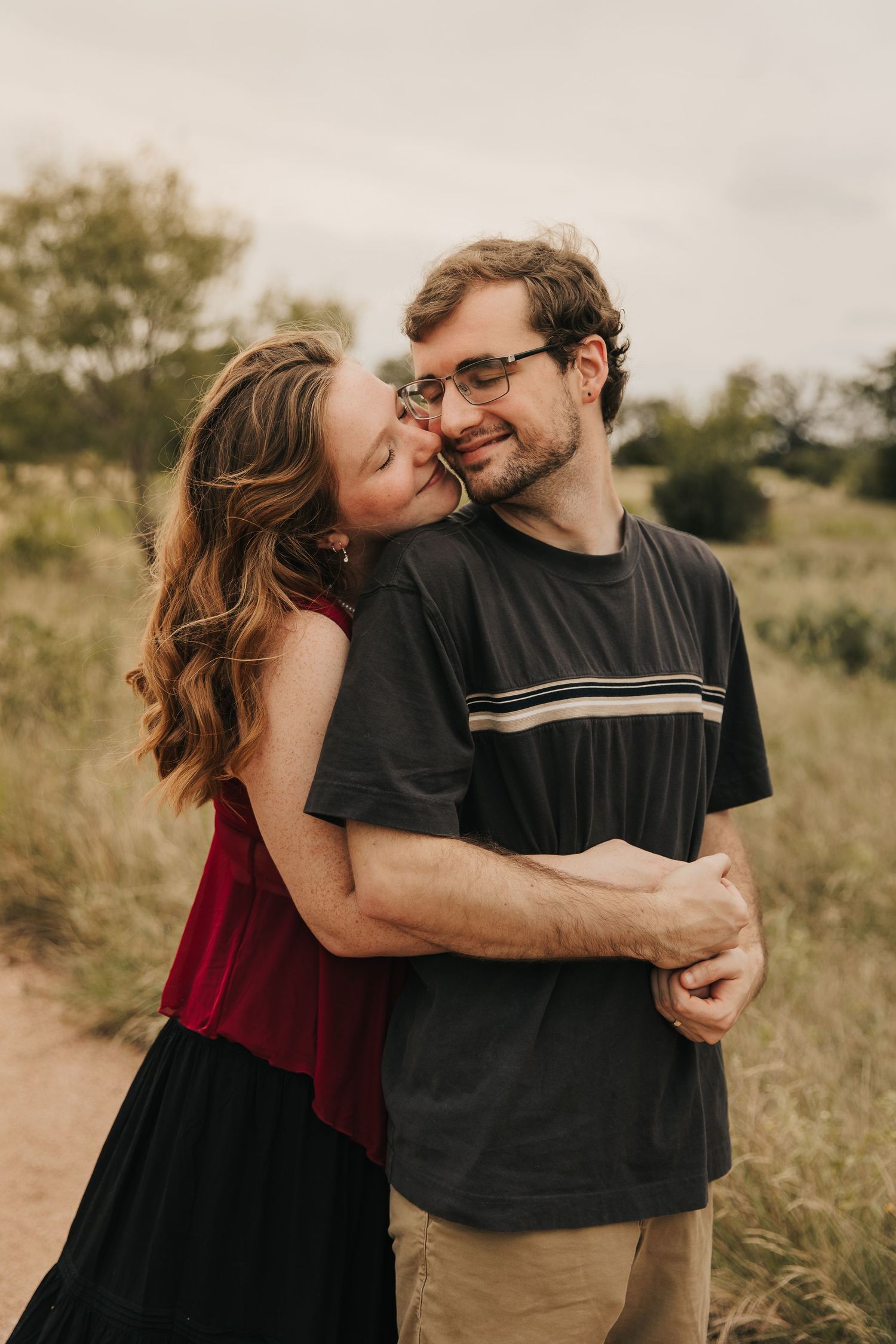 A couple embraces and shares intimate moments while standing in a field during golden hour.