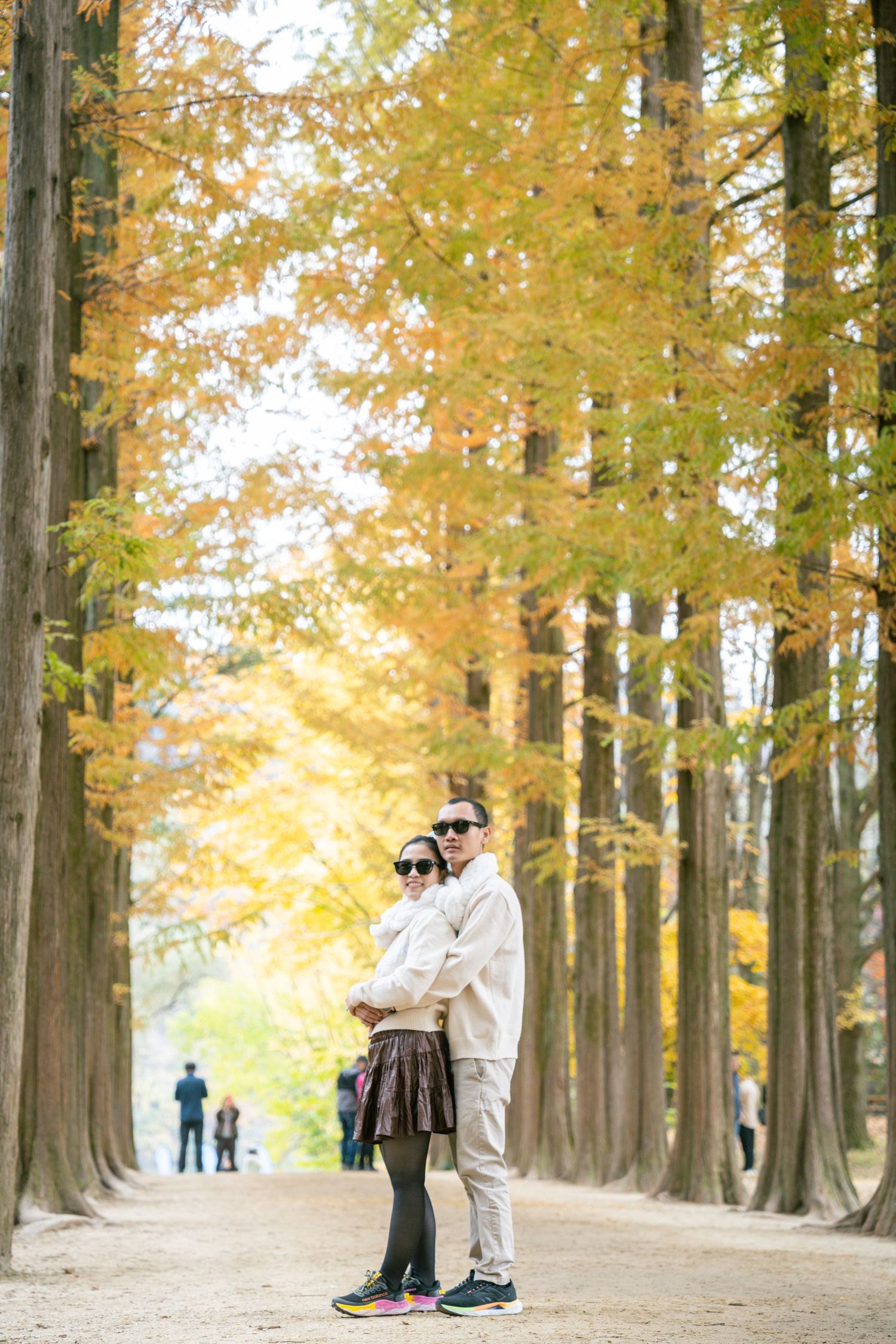 People walking along a scenic autumn path lined with tall golden ginkgo trees in the park on a fall day.