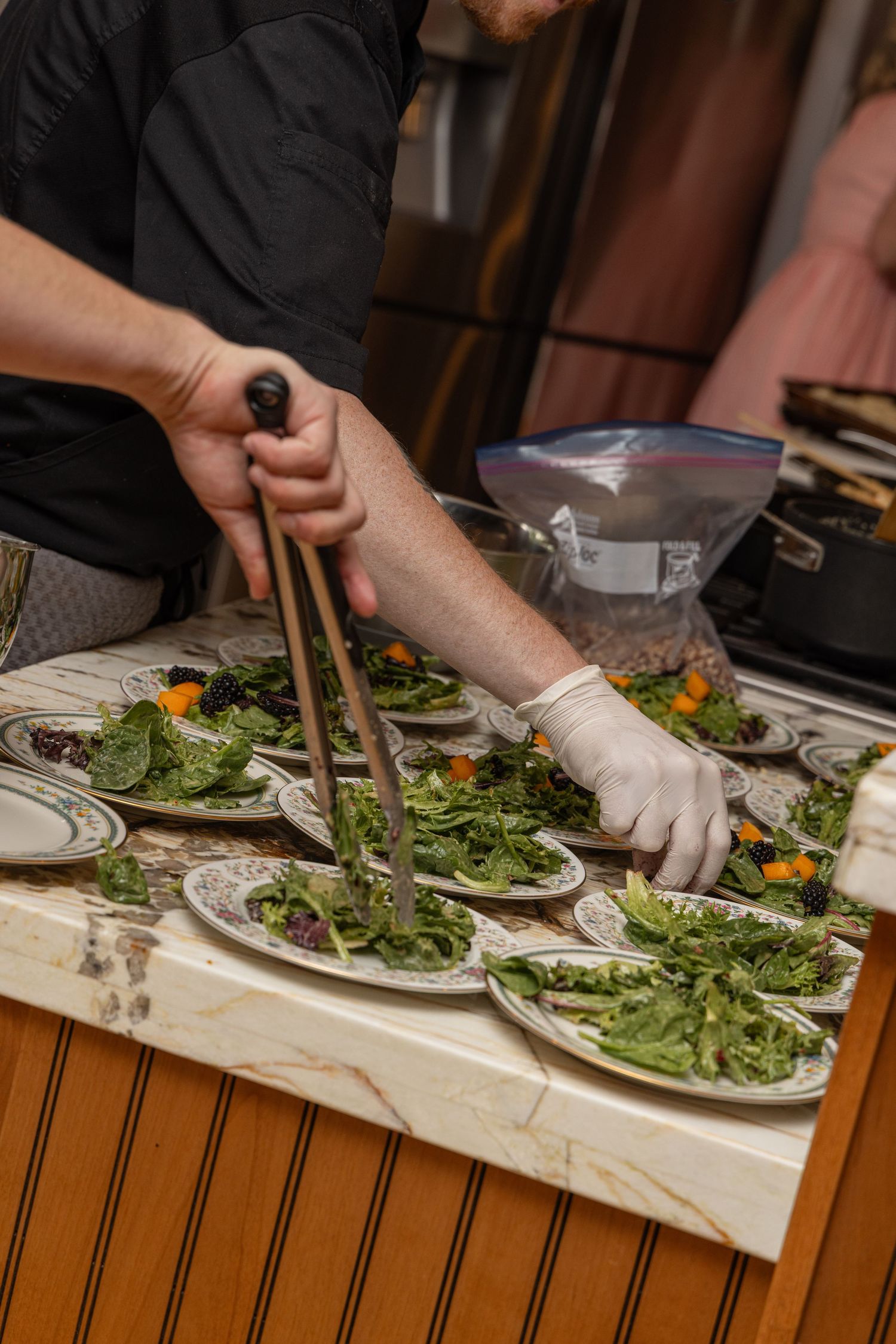 Professional chef wearing gloves plates fresh arugula salads with edible flowers in a restaurant kitchen.