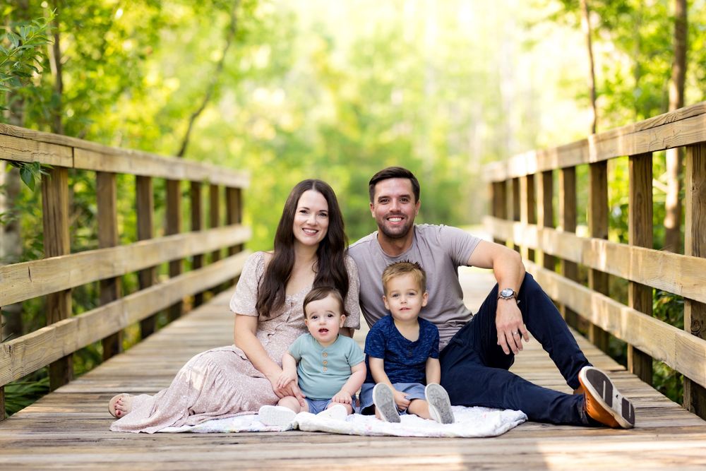 Family lying on a wooden bridge surrounded by lush greenery on a bright sunny day.