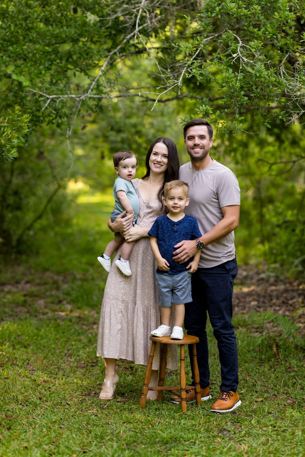 Family portrait session in a lush green garden setting with rustic wooden stool props creating a casual outdoor atmosphere.