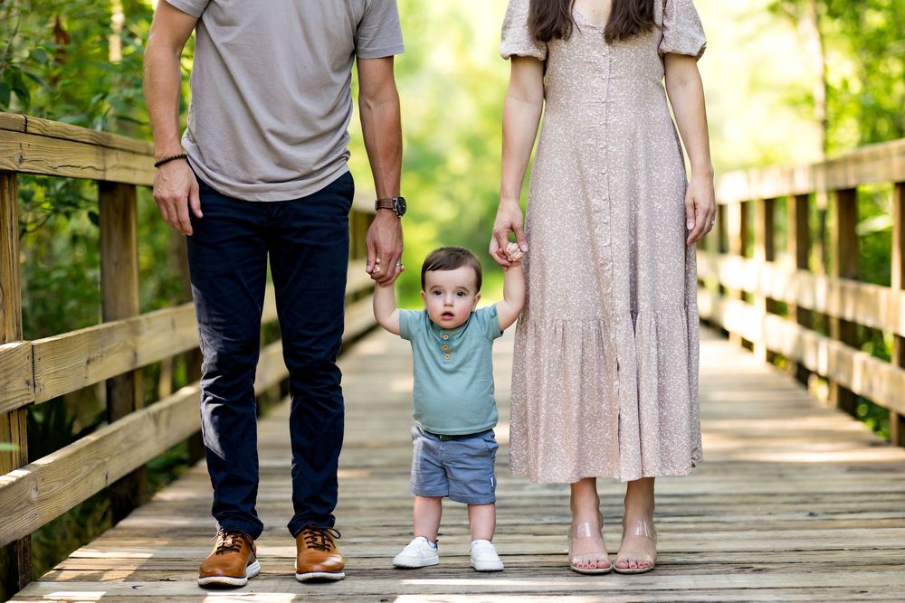 A family stands together on a wooden boardwalk or bridge in a natural outdoor setting.