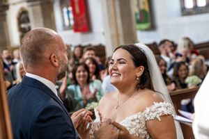 A joyful couple exchanges rings during their wedding ceremony in a church surrounded by guests.