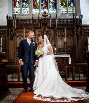 Beautiful wedding ceremony in a church with ornate wooden rood screen and stained glass windows in the background.