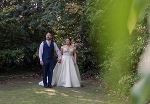 A couple walks along a garden path while surrounded by lush green foliage in an outdoor setting.