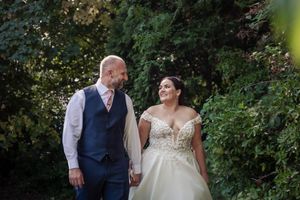 A romantic outdoor wedding photo showing a sweet embrace between a couple surrounded by lush green foliage.