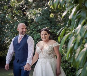 A bride and groom holding hands while walking through a lush garden setting on their wedding day.