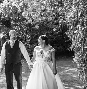 A couple in wedding attire stands together in a garden setting with lush greenery in the background.