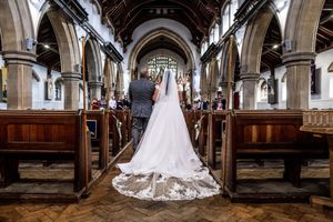 A stunning white wedding gown with a long lace train fills the center aisle of a grand traditional church interior.
