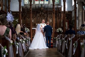 A church wedding ceremony with the couple at the altar, surrounded by decorated pews and ornate Gothic woodwork.