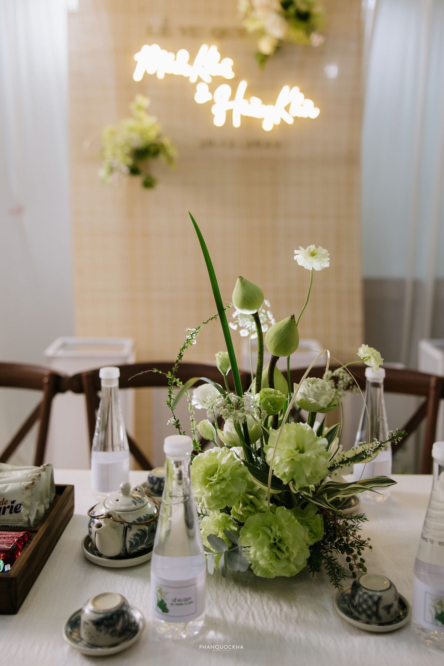Elegant wedding table centerpiece featuring green carnations, tulips, and white daisies with neon sign backdrop.
