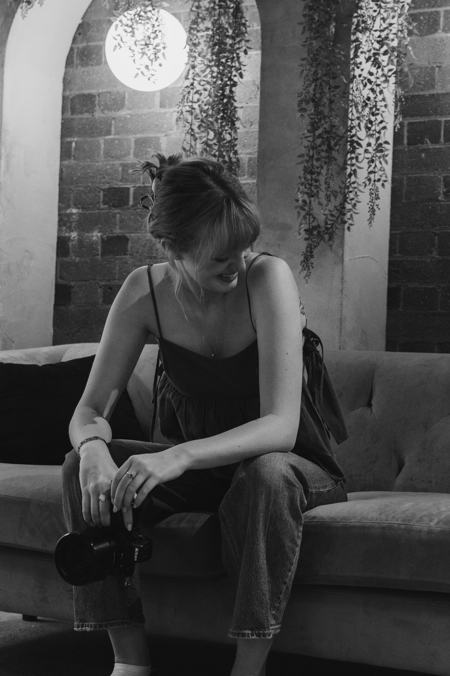 A black and white triptych of a person in dark clothing sitting on a bench against a brick wall with hanging plants.