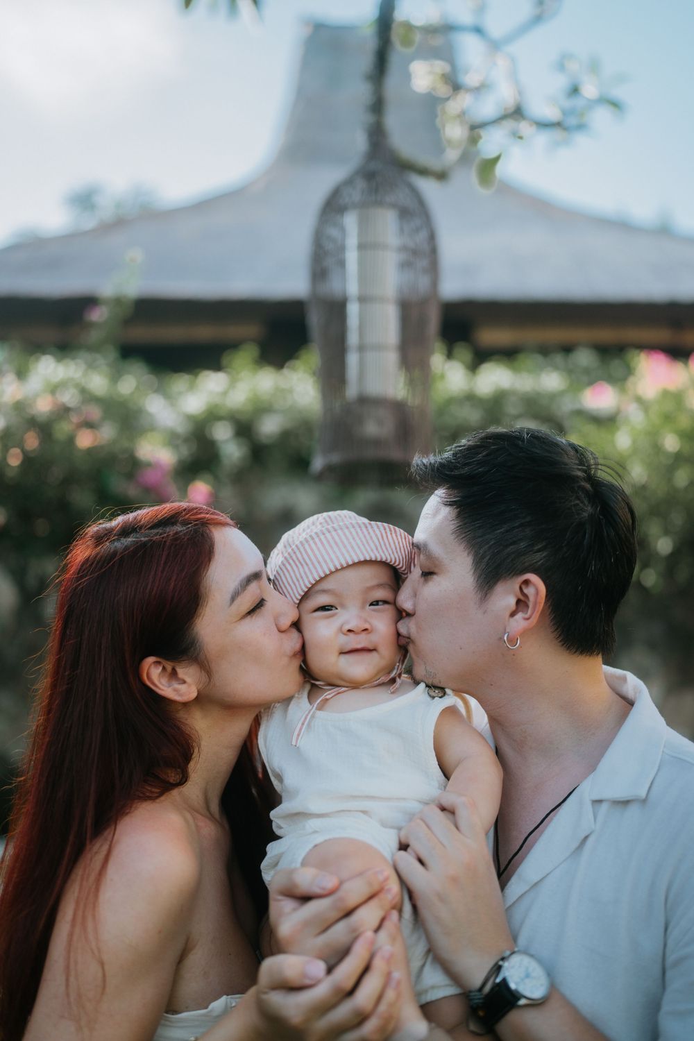 Family sharing tender moment outdoors with traditional Asian architecture in background.
