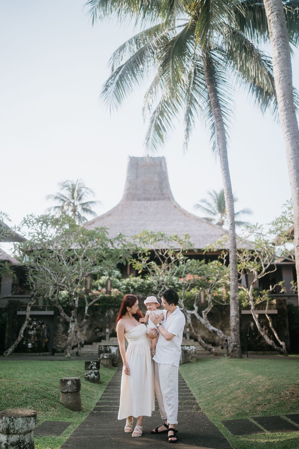 People walking along a palm tree-lined path with thatched roof buildings in the background.