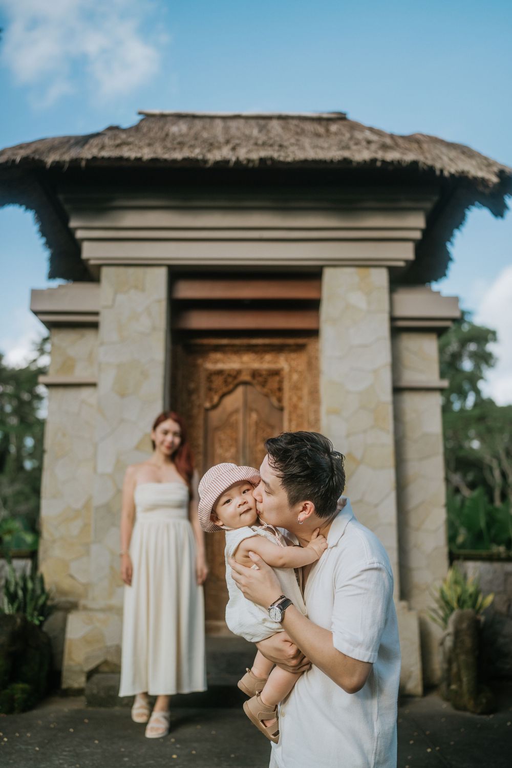 A family sharing tender moments outside a thatched-roof stone building.
