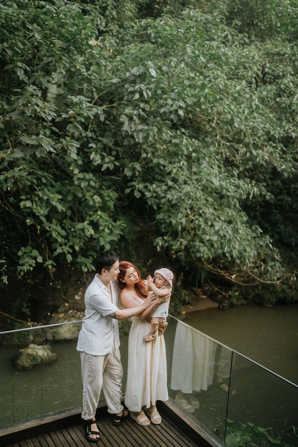 A family shares tender moments together on a wooden bridge over a tranquil stream in a lush forest setting.