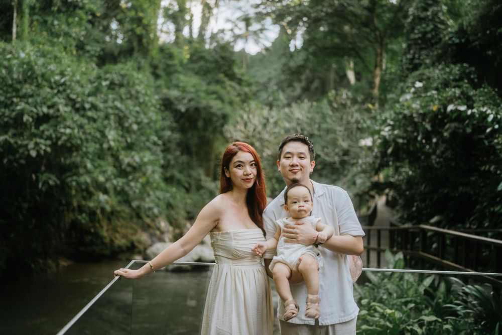 Family photoshoot on a wooden walkway surrounded by tropical greenery and water.