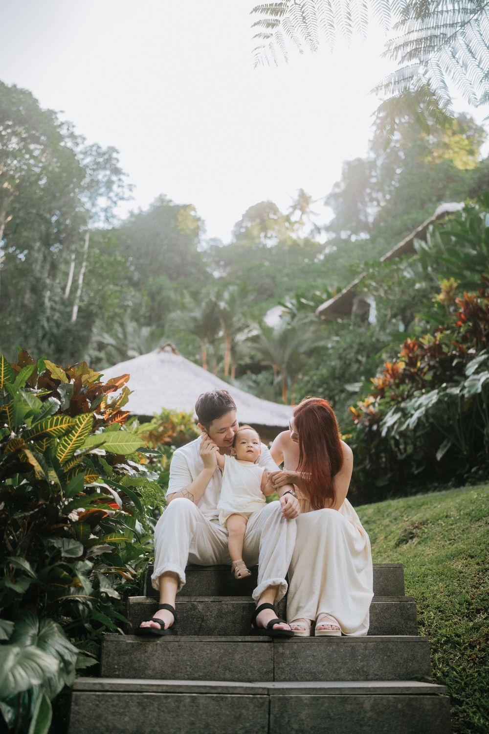 Family enjoying intimate moments together on stone steps amid tropical garden scenery.