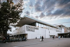 Modern white railway station building with Huvudbiblioteket signage under dramatic cloudy sky in Sweden.