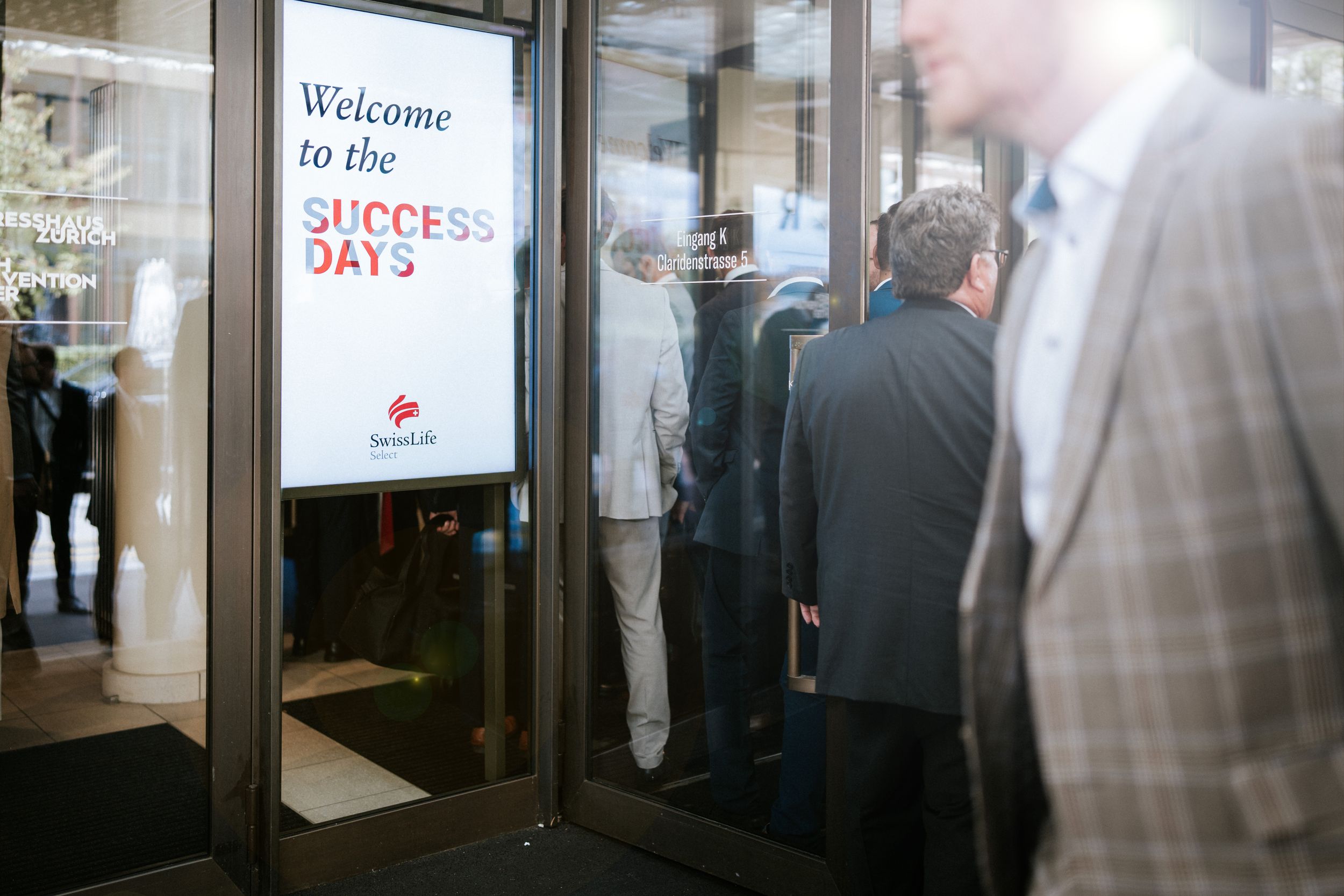 Multiple people standing in line at a counter beneath signs and illuminated displays.