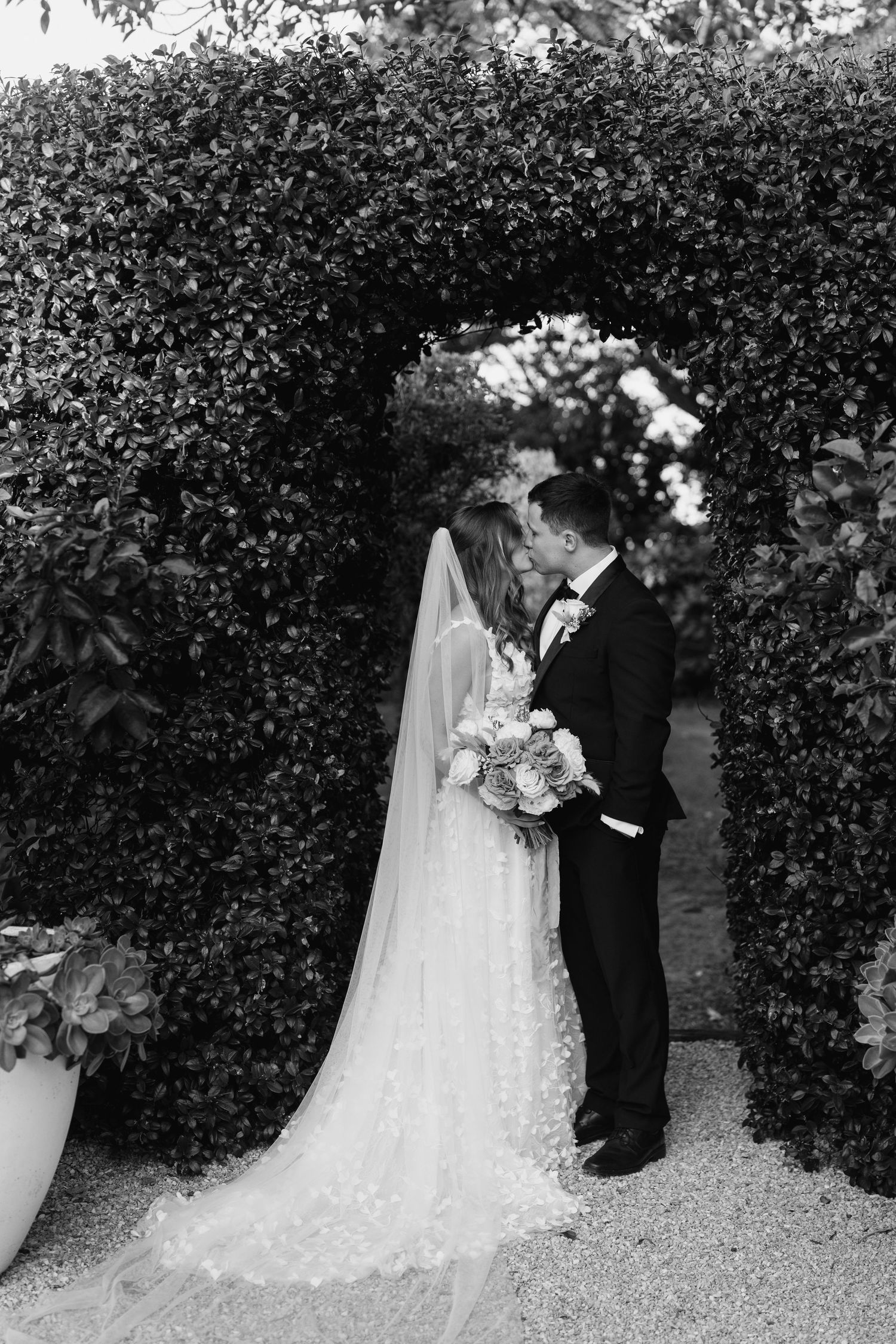 A romantic black and white wedding photography sequence showing a couple posing against a hedge backdrop in formal attire.