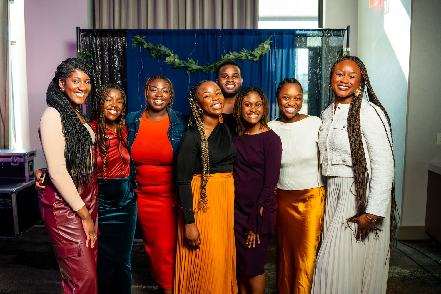 A group in colorful outfits poses together at an indoor event with curtains and decorations visible.
