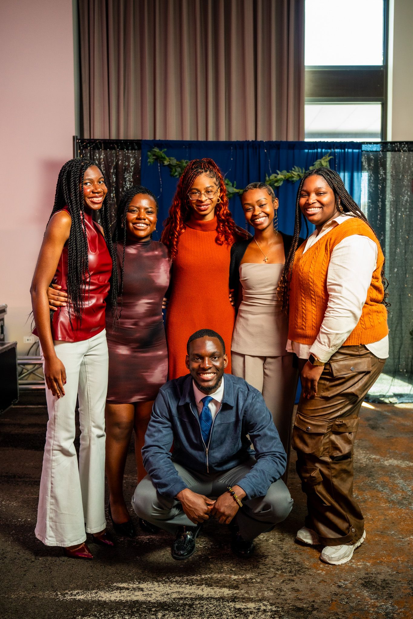 A stylish group photo showing warm earth-toned outfits against a curtained backdrop.