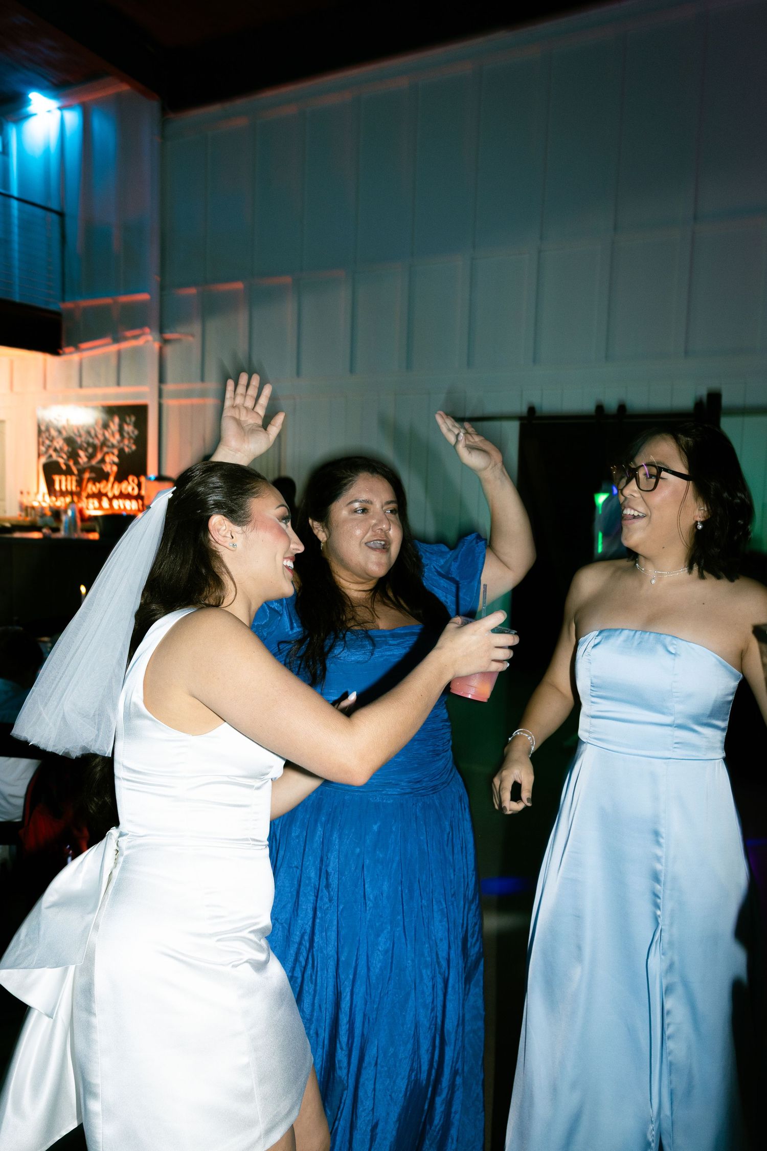 Wedding guests dancing and laughing together during a celebration in a dimly lit reception venue.