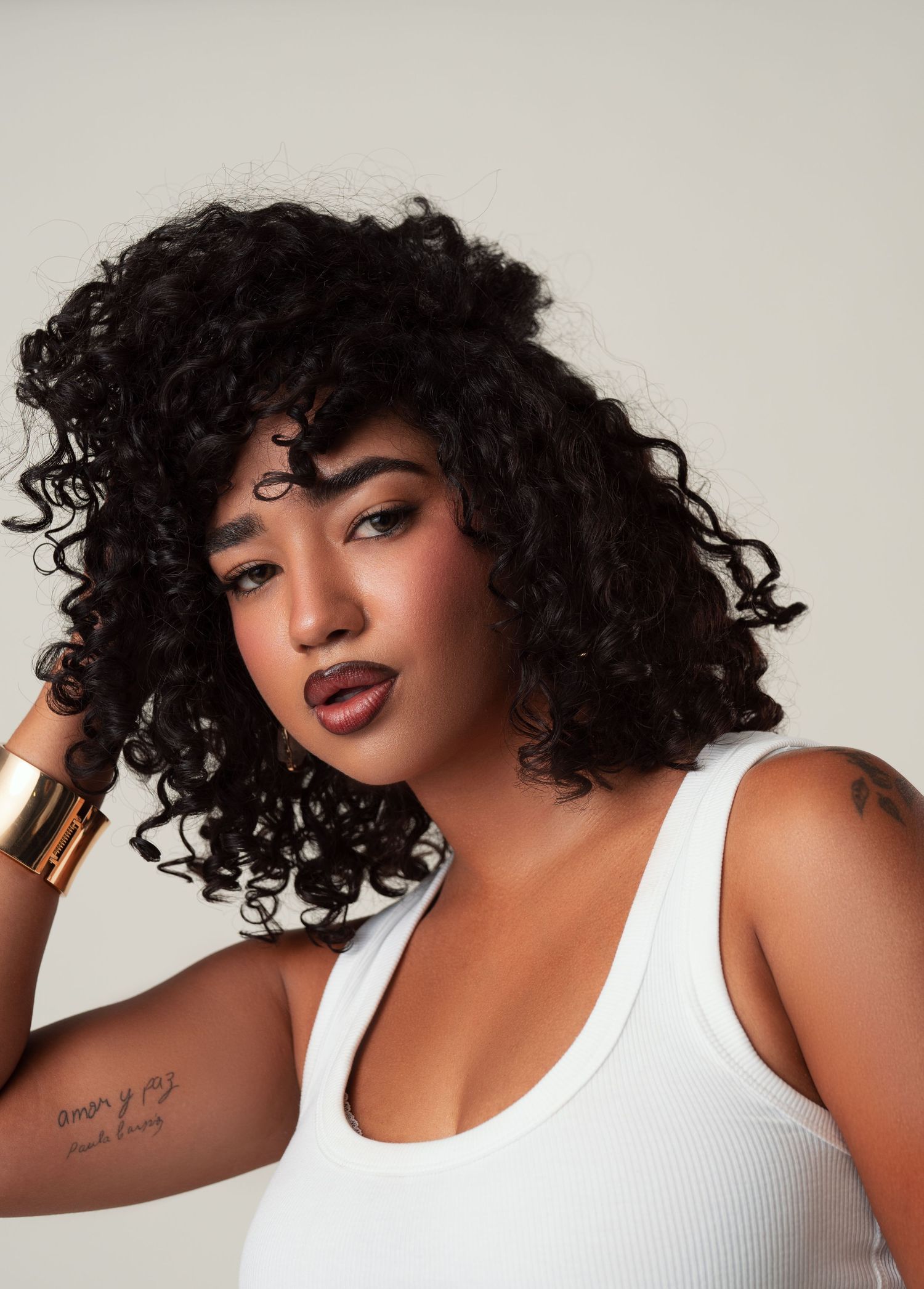 Model wearing white tank top shown from different angles with natural curly hair and bold makeup against light background.