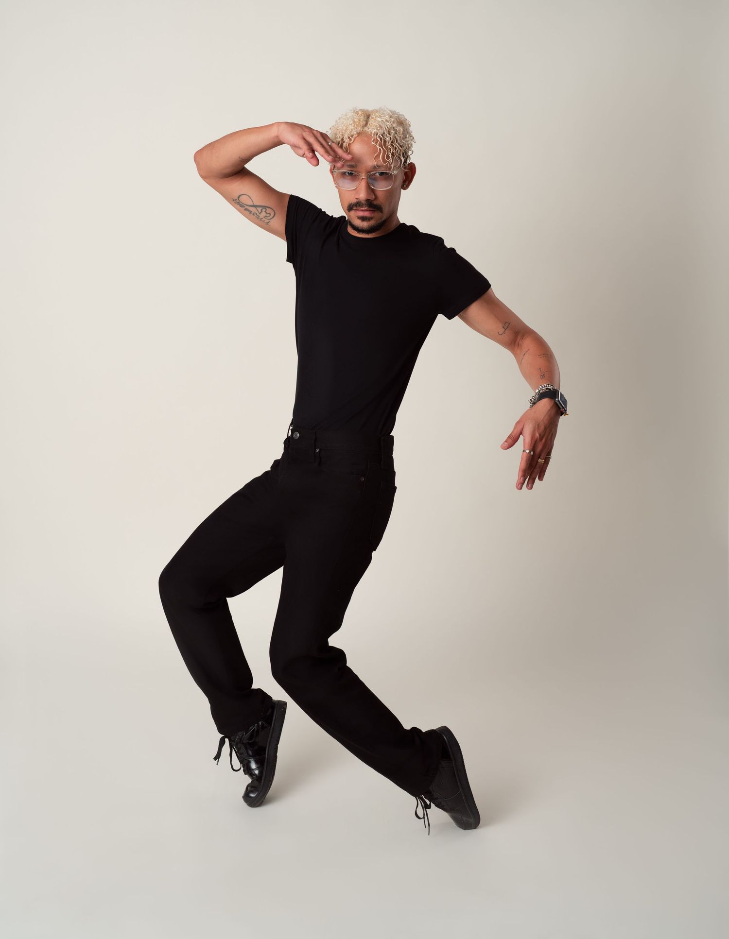 Dynamic performer wearing all black executes a dramatic dance pose against a white studio backdrop.
