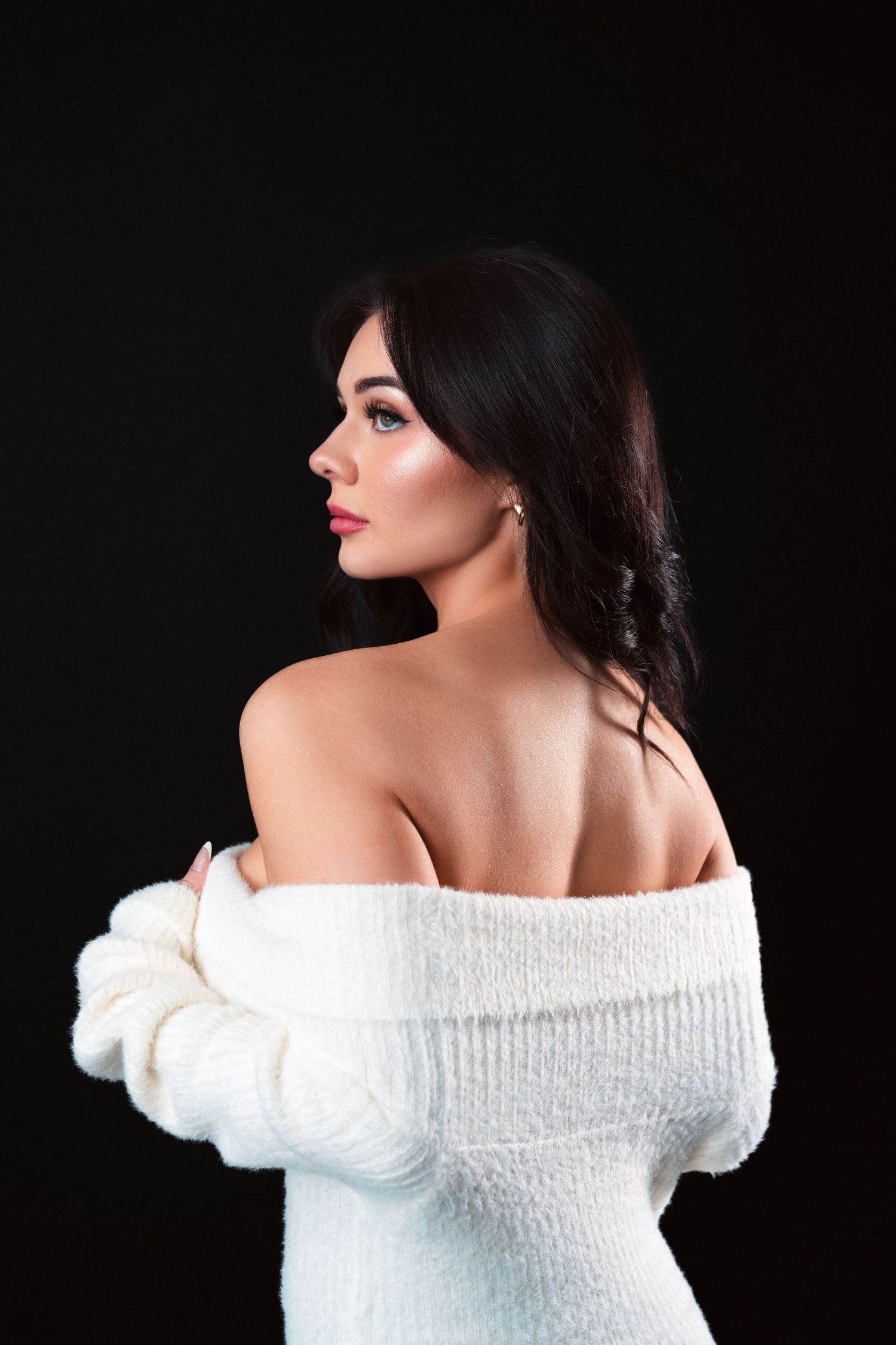 Profile view of woman wearing off-shoulder white sweater against dark background with dramatic lighting.